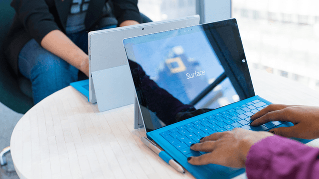 Two people using Microsoft Surface laptops at a table in a modern setting